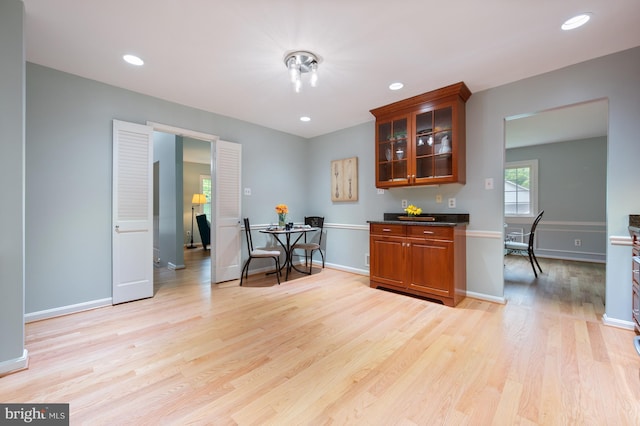 kitchen featuring recessed lighting, glass insert cabinets, baseboards, dark countertops, and light wood-style floors
