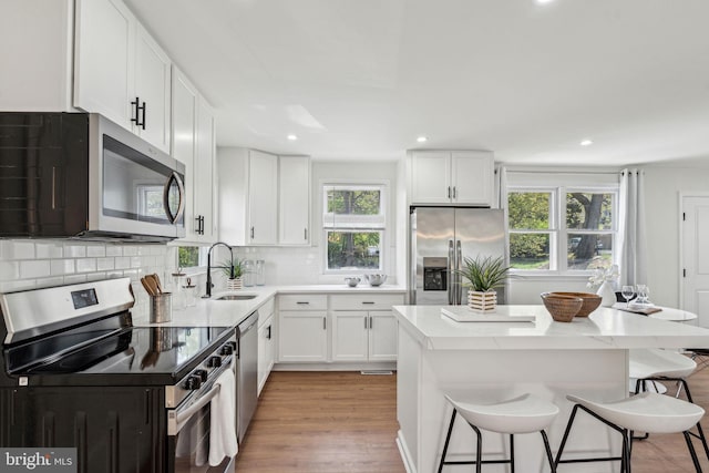 kitchen with stainless steel appliances, a sink, a kitchen breakfast bar, light wood-style floors, and recessed lighting