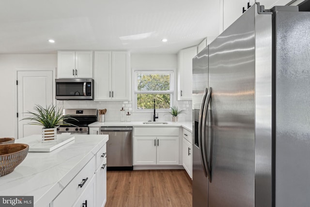 kitchen with appliances with stainless steel finishes, a sink, backsplash, white cabinets, and recessed lighting