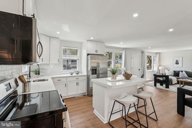 kitchen with stainless steel appliances, light wood-style floors, recessed lighting, backsplash, and a breakfast bar area