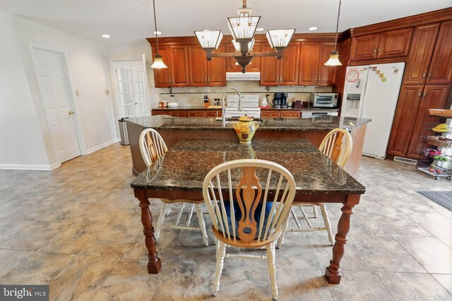 kitchen featuring white appliances, under cabinet range hood, a kitchen island with sink, baseboards, and a kitchen bar