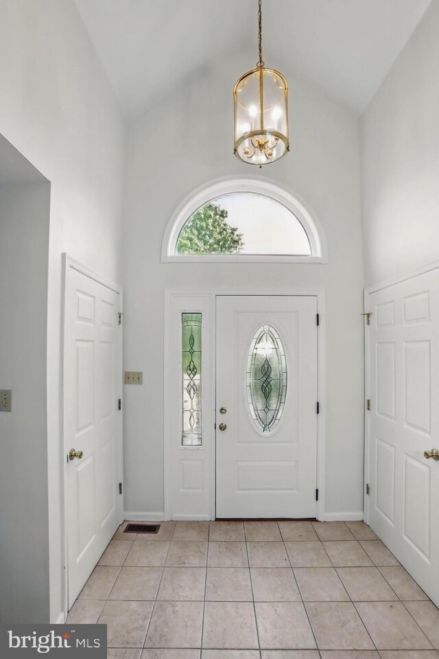 entryway featuring a high ceiling, healthy amount of natural light, light tile patterned floors, a chandelier, and baseboards