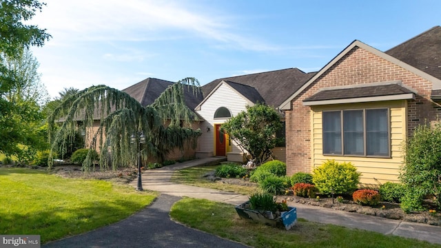 view of front facade with a front lawn, brick siding, and roof with shingles