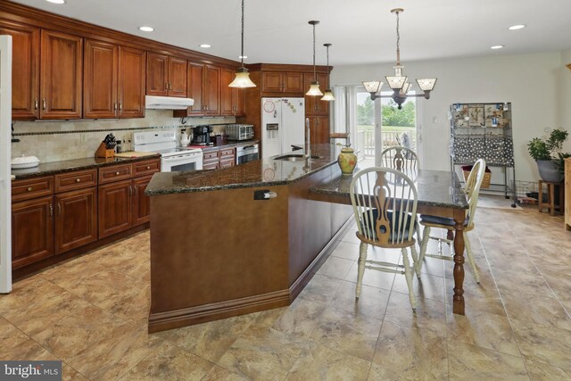 kitchen with white appliances, under cabinet range hood, an island with sink, a chandelier, and recessed lighting