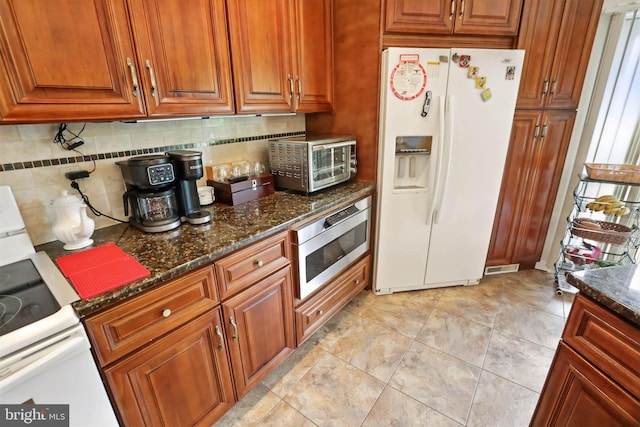 kitchen featuring white appliances, tasteful backsplash, dark stone counters, and brown cabinets