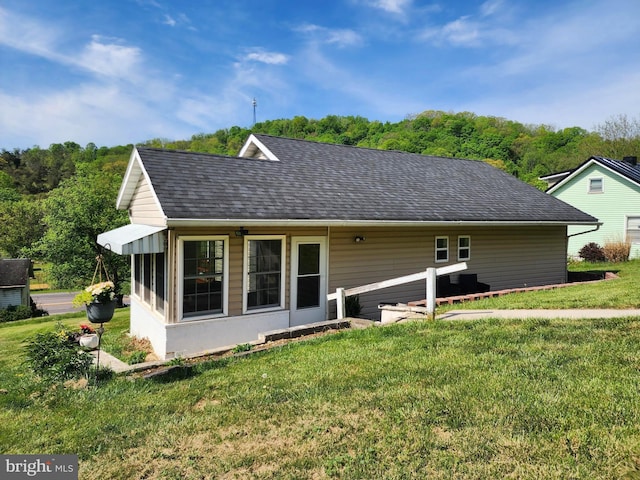 rear view of house featuring a lawn and roof with shingles