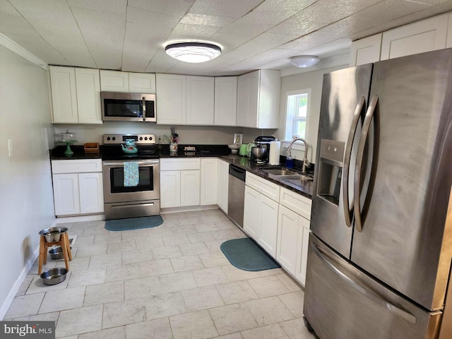kitchen with a sink, stainless steel appliances, dark countertops, and white cabinets