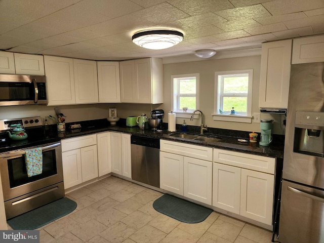kitchen featuring white cabinets, appliances with stainless steel finishes, dark stone counters, and a sink