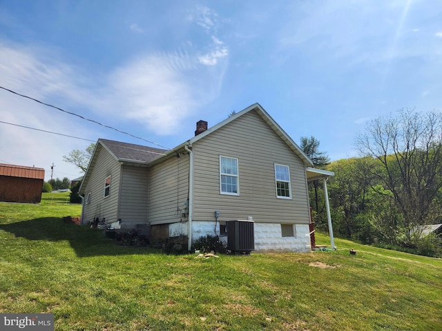 view of side of property with central AC unit, a chimney, and a lawn