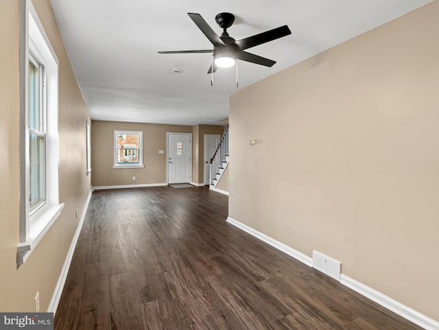 unfurnished living room with baseboards, dark wood-style flooring, ceiling fan, visible vents, and stairway