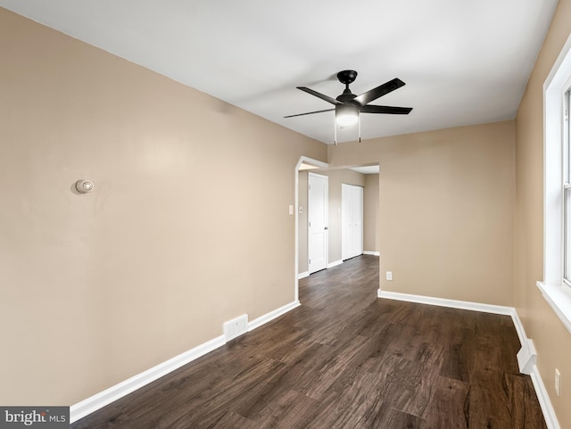 unfurnished room with ceiling fan, baseboards, dark wood-type flooring, and visible vents