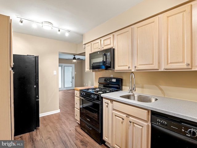 kitchen featuring light brown cabinets, a sink, wood finished floors, black appliances, and light countertops