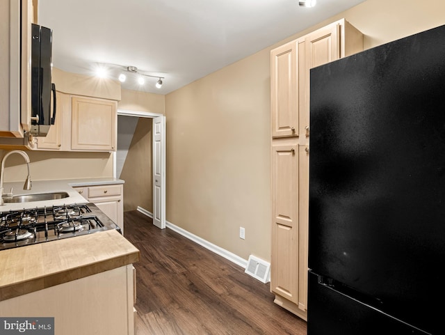 kitchen featuring a sink, freestanding refrigerator, visible vents, dark wood-style flooring, and baseboards