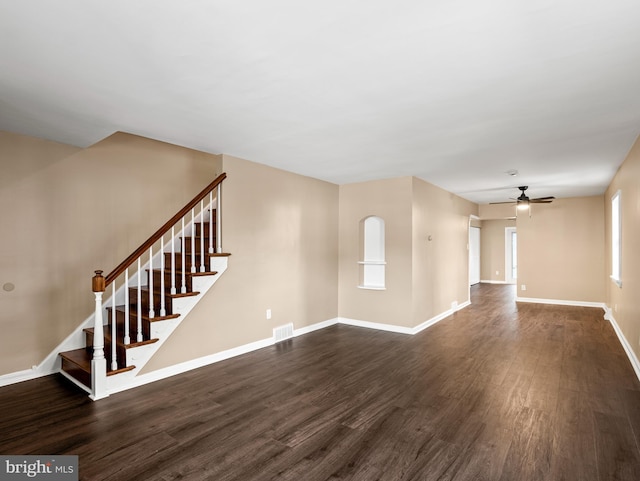 unfurnished living room featuring a ceiling fan, stairs, dark wood-type flooring, and visible vents
