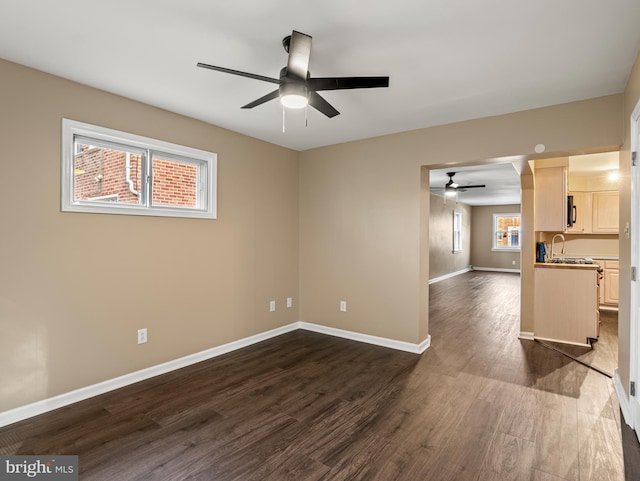 unfurnished living room featuring dark wood-style flooring, baseboards, ceiling fan, and a sink