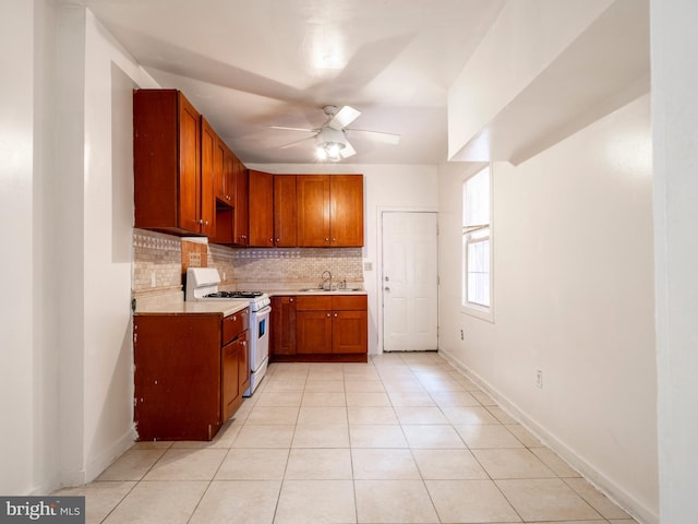 kitchen featuring gas range gas stove, a sink, a ceiling fan, tasteful backsplash, and light countertops