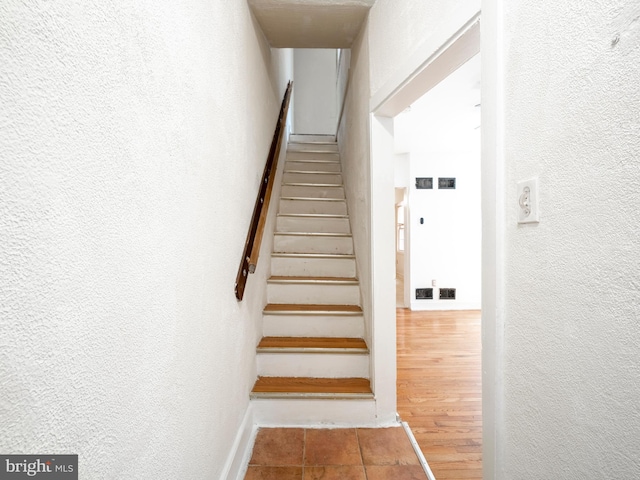 staircase with a textured wall, baseboards, and tile patterned flooring