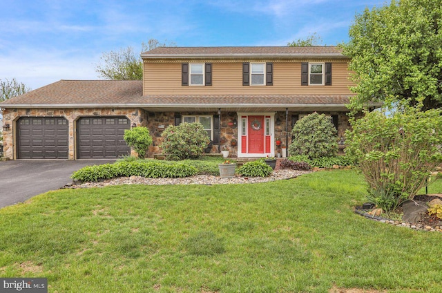 traditional-style house with an attached garage, stone siding, a front lawn, and aphalt driveway
