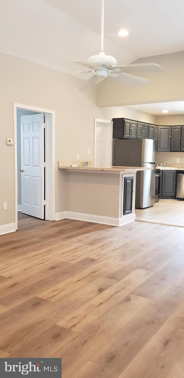 unfurnished living room featuring light wood finished floors, baseboards, a ceiling fan, and a sink