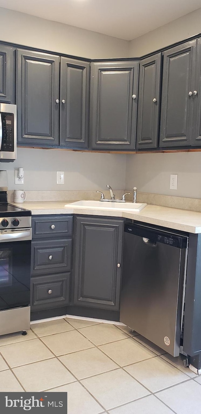 kitchen featuring light countertops, a sink, appliances with stainless steel finishes, and light tile patterned flooring