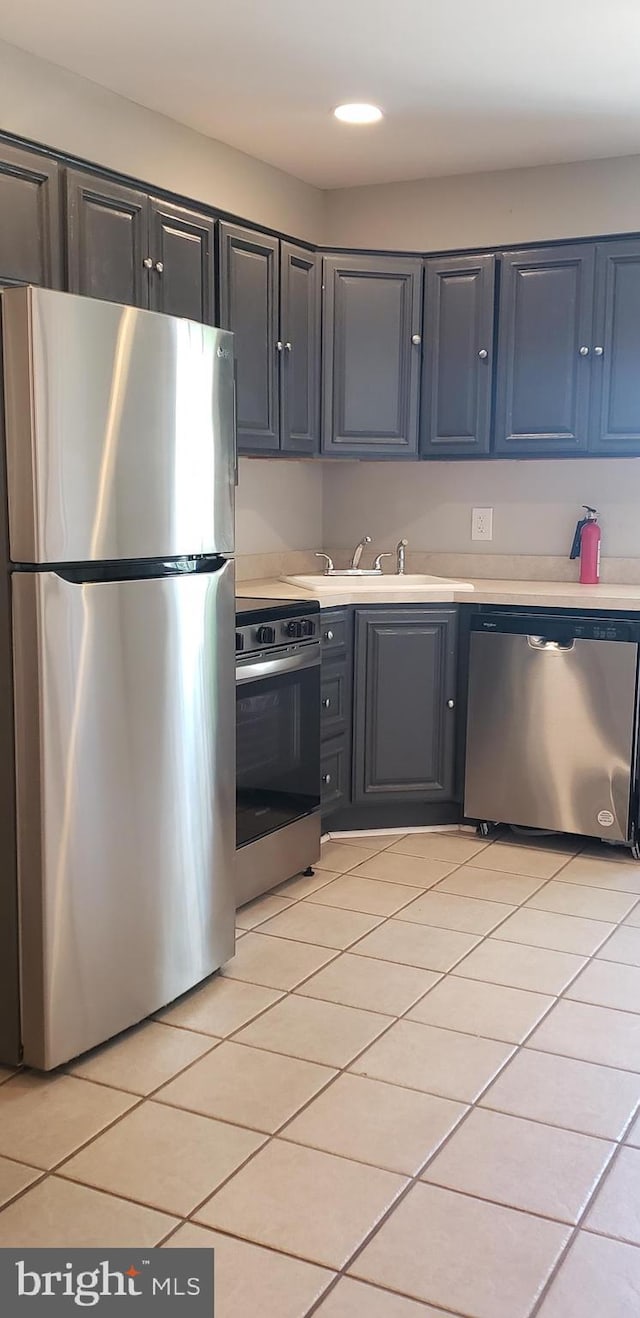 kitchen with a sink, stainless steel appliances, light tile patterned flooring, and light countertops