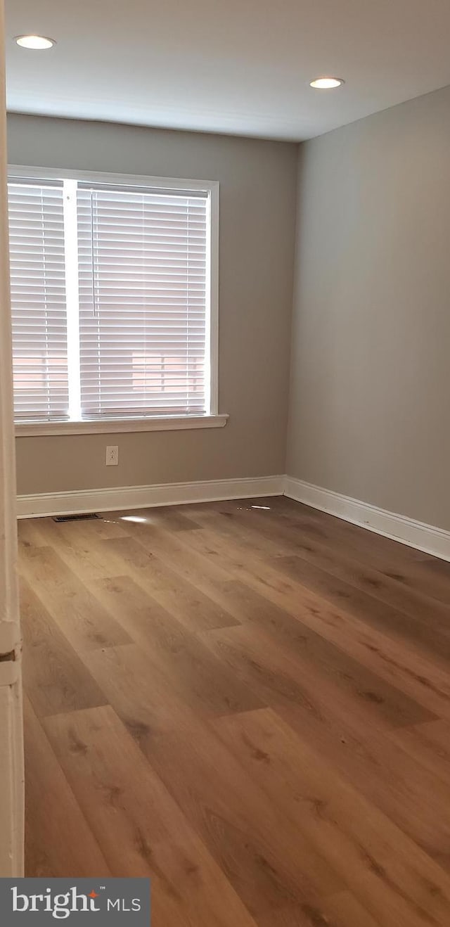 empty room featuring a wealth of natural light, wood finished floors, baseboards, and recessed lighting