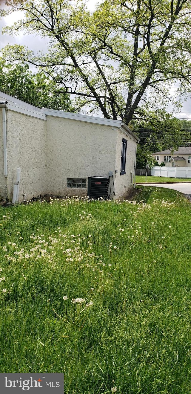 view of side of home with central air condition unit, stucco siding, and fence