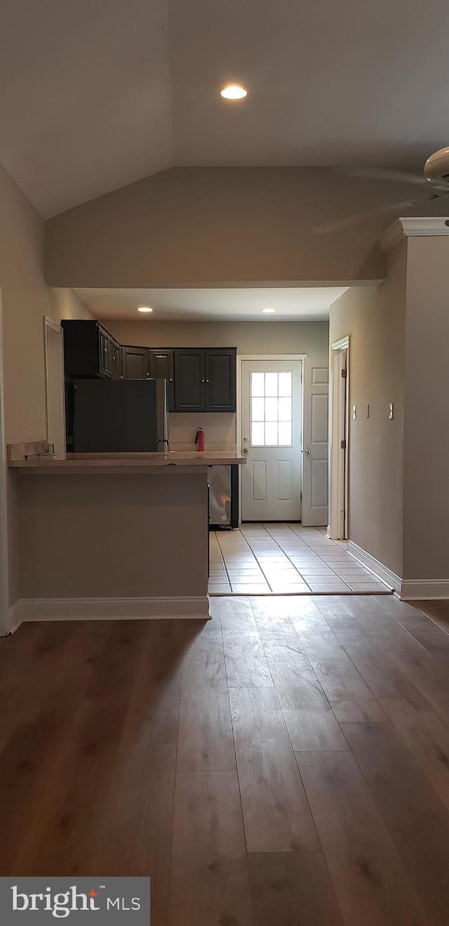 kitchen featuring light wood finished floors, a peninsula, dishwashing machine, refrigerator, and lofted ceiling