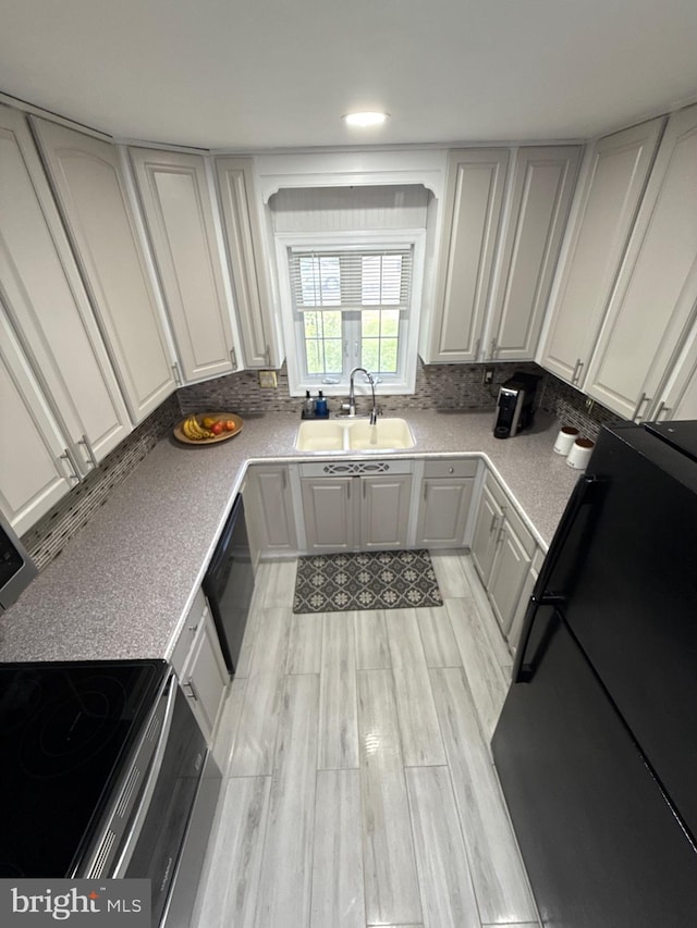 18 River Ln, Levittown, PA 19055 - kitchen featuring a sink, black appliances, decorative backsplash, and light wood finished floors