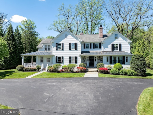 view of front of home featuring a porch, a chimney, a front lawn, a standing seam roof, and metal roof