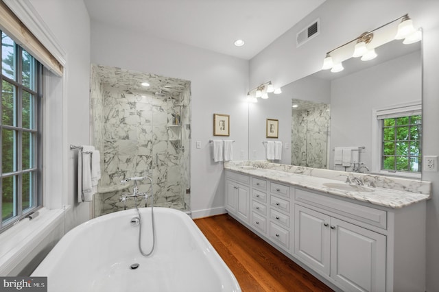 full bath with a marble finish shower, a freestanding tub, wood finished floors, and double vanity