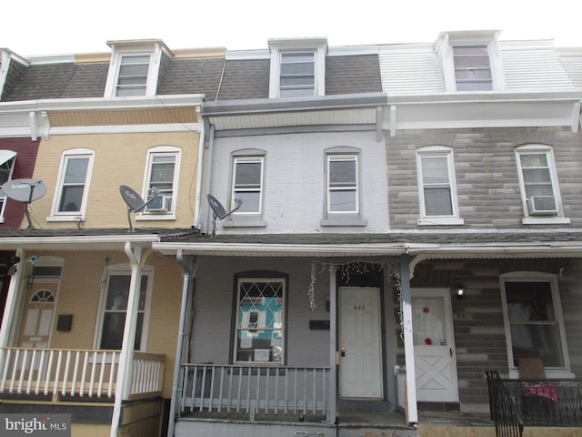 multi unit property featuring mansard roof, a porch, brick siding, and roof with shingles