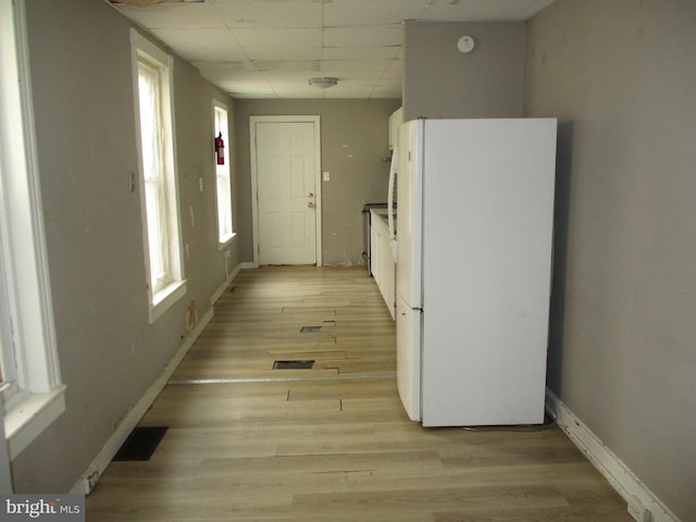 hallway featuring light wood finished floors, baseboards, visible vents, and a drop ceiling
