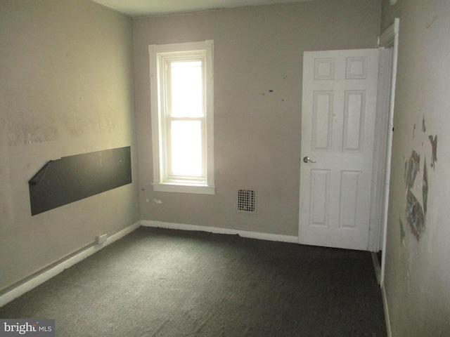 spare room featuring visible vents, baseboards, and dark colored carpet