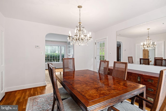 dining space featuring arched walkways, a chandelier, wood finished floors, and baseboards