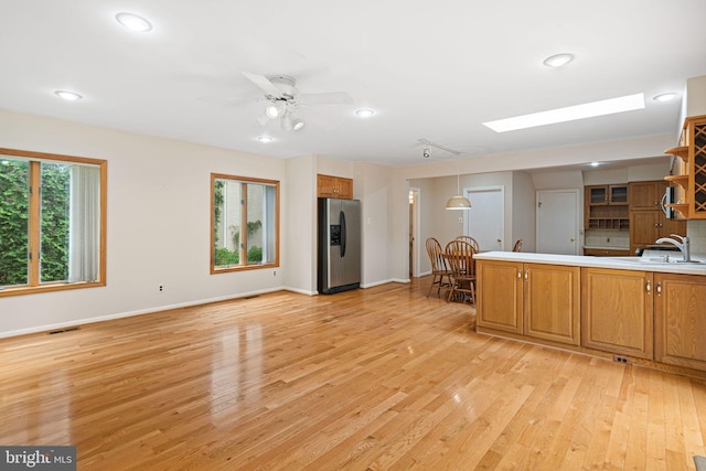 kitchen featuring stainless steel refrigerator with ice dispenser, light wood finished floors, a sink, baseboards, and a peninsula