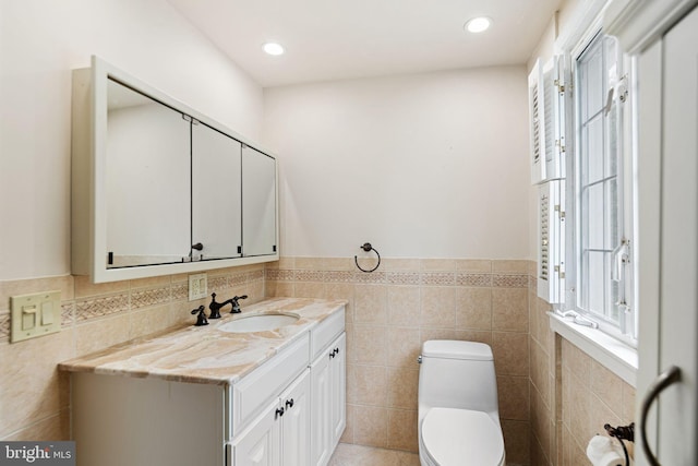 half bathroom with toilet, tile walls, a wainscoted wall, vanity, and healthy amount of natural light