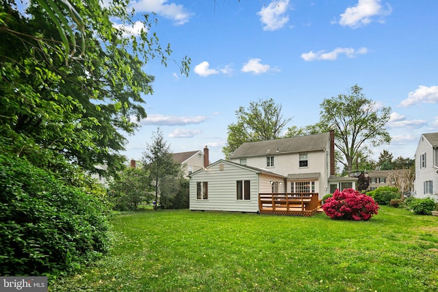 rear view of house featuring a wooden deck, a lawn, and a chimney
