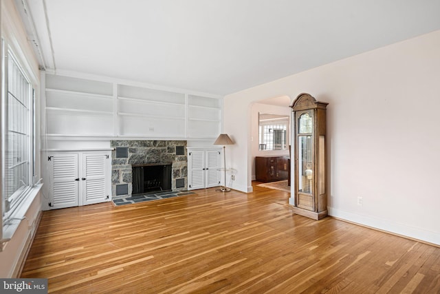 unfurnished living room with wood finished floors, baseboards, a stone fireplace, and built in shelves