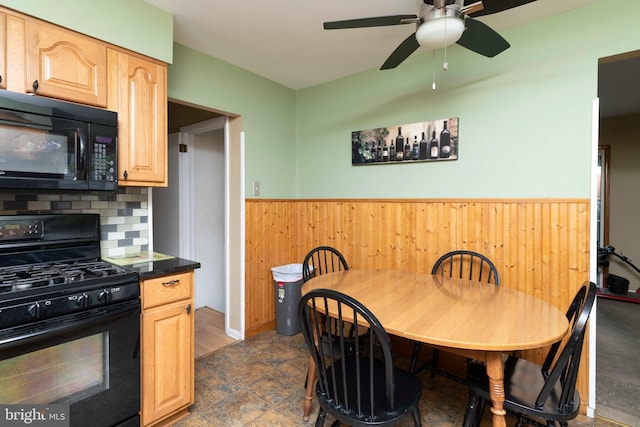 dining space featuring a ceiling fan, wooden walls, and wainscoting