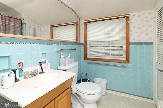 bathroom featuring lofted ceiling, tile walls, wallpapered walls, toilet, and vanity