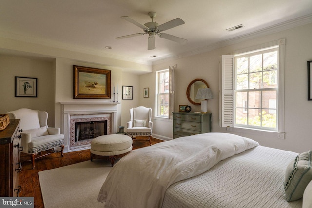 bedroom featuring crown molding, a fireplace with raised hearth, dark wood-style flooring, and a ceiling fan