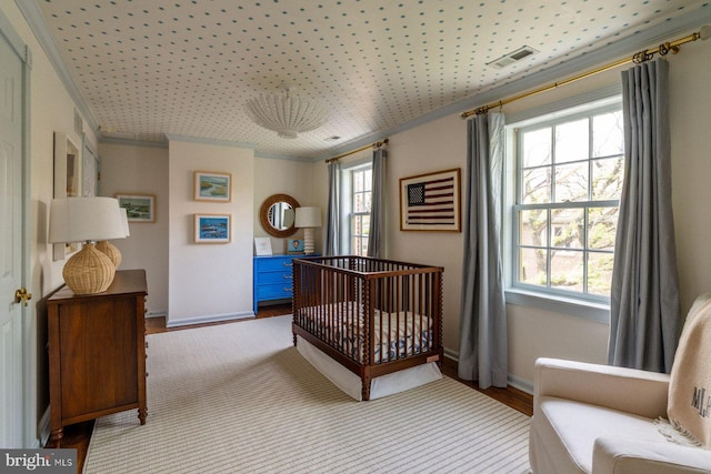 bedroom featuring light wood finished floors, baseboards, ornamental molding, and a crib