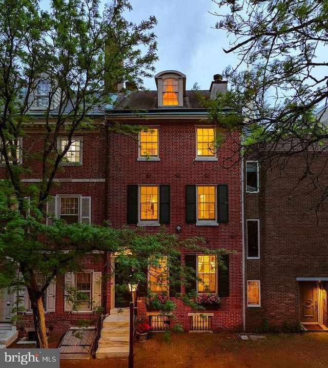 rear view of house featuring a chimney and brick siding