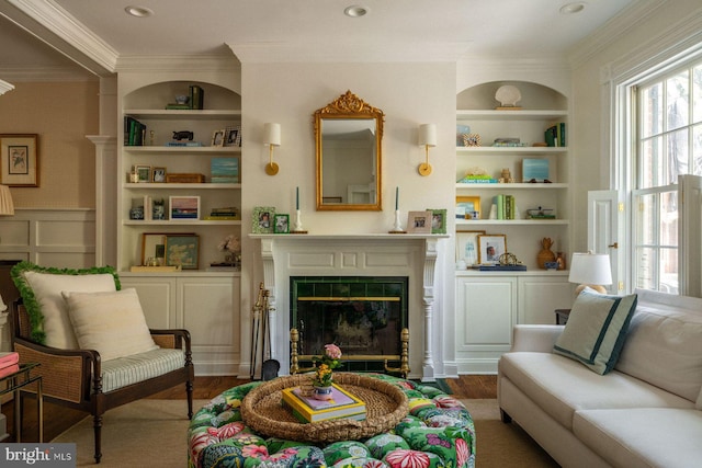 living area featuring ornamental molding, built in features, healthy amount of natural light, a fireplace with flush hearth, and wood finished floors