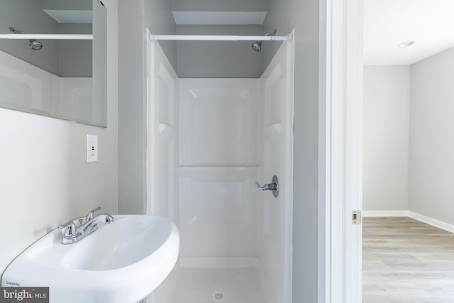 bathroom with a shower, wood finished floors, baseboards, and a sink