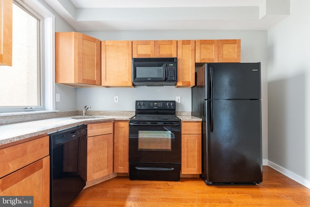 kitchen with light wood-style floors, baseboards, black appliances, and a sink