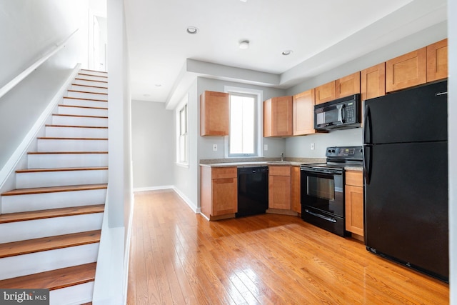 kitchen with a sink, black appliances, light wood-style flooring, light countertops, and baseboards