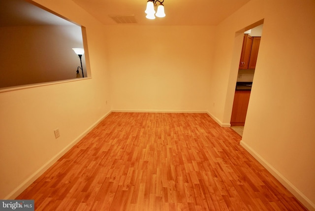 empty room with an inviting chandelier, light wood-style floors, visible vents, and baseboards