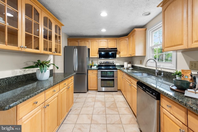 kitchen with stainless steel appliances, a sink, glass insert cabinets, dark stone countertops, and recessed lighting